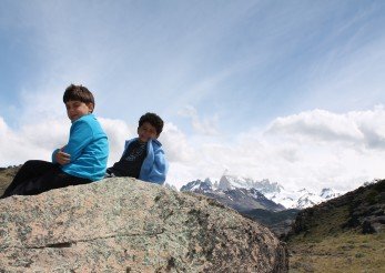 duas crianças sentadas numa pedra com montanhas nevadas ao fundo