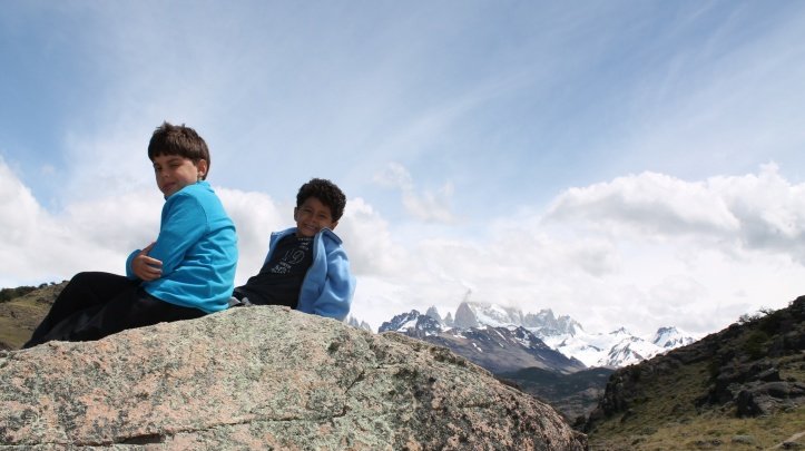duas crianças sentadas numa pedra com montanhas nevadas ao fundo