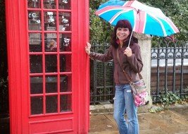 Mulher com guarda-chuva em frente a cabine telefônica londrina
